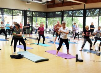 Coppell Senior and Community Center promotes healthy aging Group of males and females doing pilates in a window-lined room.