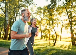 Why immunisation matters for healthy ageing Cardio training outdoors. Side view of caucasian grey bearded man and beautiful old woman running along summer park with sunlight on background. Cheerful retired people leading active lifestyle.