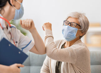 Two-thirds of US adults self-monitor heart health Cheerful older woman bumping elbows with healthcare worker. Both are wearing masks.