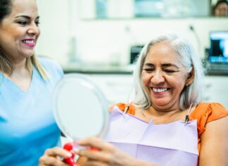 4 Common Oral Health Changes Caused by Aging, and How to Prevent Them Older woman holding mirror at the dentist